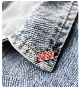 Close-up of Self Love Club ticket enamel pin on denim jacket with retro pink design