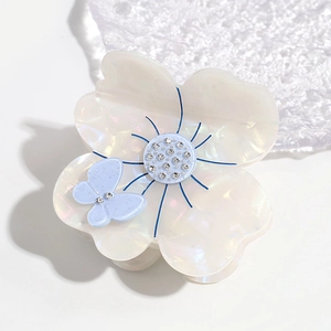 Detailed shot of pearlescent white flower hair claw clip with blue butterfly and rhinestones