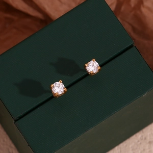 Close-up of gold stud earrings with round white zircon on a dark green jewelry box