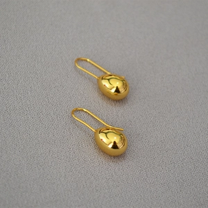 Macro shot of minimalist gold drop earrings with a polished finish on textured fabric