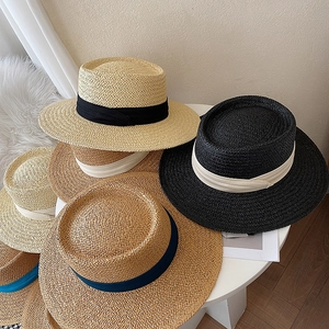 Detail view of woven straw boater hats in beige, black, and brown with ribbon bands