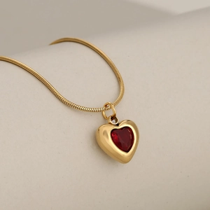 Elegant gold snake chain necklace with a ruby red heart pendant on a white pedestal