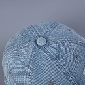 Dettaglio della corona del berretto da baseball in denim azzurro con bottone e occhielli