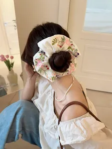 Detailed view of a white satin hair scrunchie with floral embroidery on a low bun hair style