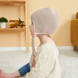 Detail shot of beige knit baby hat with earflaps and braided ties on child model