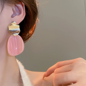 Detail view of irregular pink resin earrings with golden wave texture on a female model