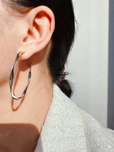 Macro side view of large silver twisted hoop earrings worn by a model in natural light