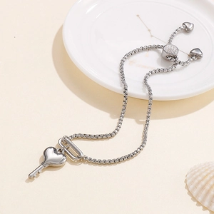 Adjustable silver box chain bracelet with heart key charm on a minimalist white ceramic plate