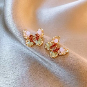 Close-up of butterfly stud earrings with colorful crystals on champagne silk background