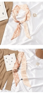 Flat lay of pink silk scarf with floral pattern and letter L detail on knit sweater