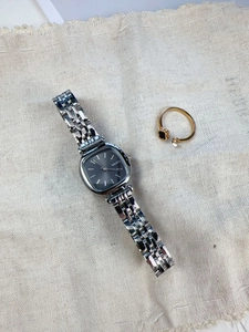 Close-up of square black dial watch with silver steel band and clover ring on fabric