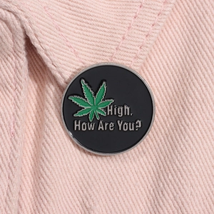 Macro detail of a round enamel pin featuring a green leaf and High How Are You text
