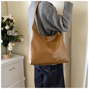 Brown glossy leather hobo bag shown on shoulder with elegant drape and minimalist style