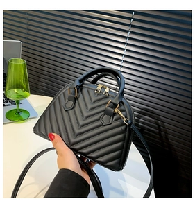 Detail of black V-quilted faux leather shell bag with gold zippers and sturdy dual handles