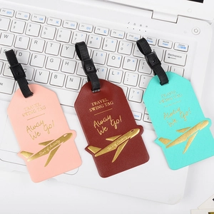Close-up of three faux leather travel tags in pink, burgundy, and teal on a laptop