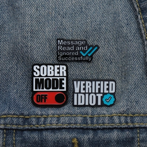 Trois pin's en émail avec textes humoristiques sur denim, incluant Message Read et Idiot