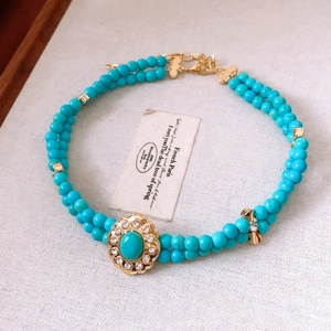 Dettaglio collana doppia a perline turchesi con ciondolo a fiore dorato e strass
