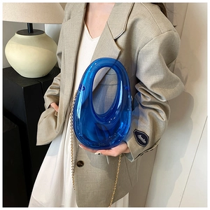 Detail of blue acrylic ring handbag with gold chain strap held by a fashion model