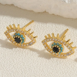 Close-up of golden evil eye stud earrings with cubic zirconia and turquoise inlay