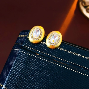 Detailed view of oval gold earrings with large central stone and micro-diamond pavé border