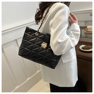 Dettaglio della grande borsa tote trapuntata nera con catena su un blazer bianco