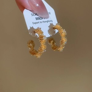 Macro view of gold-plated C-shaped earrings with textured surface and cubic zirconia accents