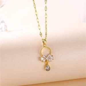 Golden bow pendant necklace with teardrop zircon on a minimalist beige background