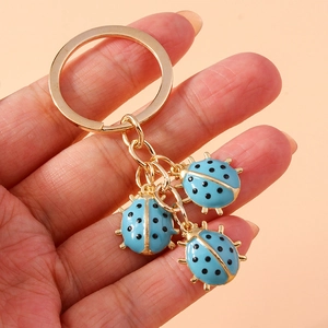 Close-up of golden keychain with three blue enamel ladybug charms held by a hand