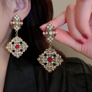 Close-up of Baroque earrings with red gems, pearls and crystals on golden metal