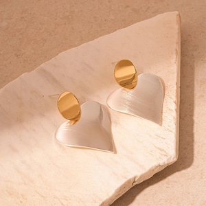 Detail of gold and silver heart earrings showing horizontal brushed metal texture on stone