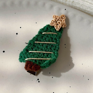 Detail of hand-knitted green wool Christmas tree hair clip with gold thread on ceramic tray
