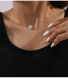 Detailed close-up of white shell flower pendant on a golden beaded chain necklace