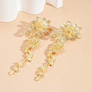 Macro shot of gold floral earrings with intricate leaf patterns and sparkling crystals