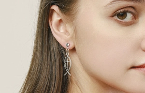 Close-up of silver titanium steel fish earrings featuring a Jesus cross design worn by model