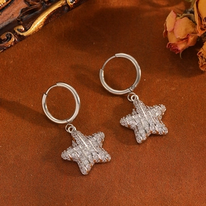 Detail shot of silver hoop earrings with shimmering crystal star pendants on brown cloth