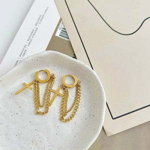 Golden cross and tassel chain earrings in titanium steel displayed on a ceramic tray