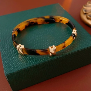 Detailed close-up of leopard resin bangle with gold X-shaped metal accent on box