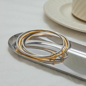 Détail de bracelets entrelacés or et argent sur un plateau en métal au style épuré