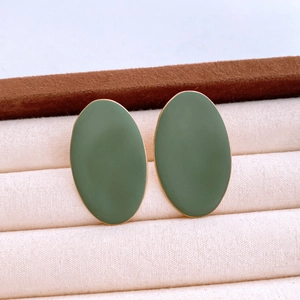Close-up of green oval matte earrings with golden metal borders on soft beige velvet