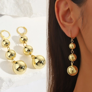 Macro shot of gold tiered triple ball drop earrings with lever-back closure on model