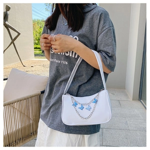 Detail of white shoulder bag featuring silver metal chain and blue butterfly pendant