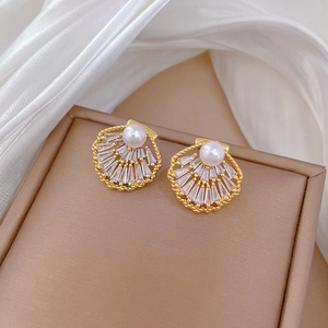 Macro shot of gold fan-shaped stud earrings with sparkling crystals and a central pearl