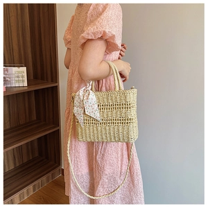 Straw woven handbag with floral scarf and long strap shown on shoulder with lace dress