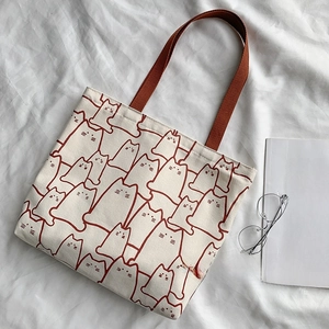 Detail shot of canvas tote bag with cat patterns and woven brown handles on fabric