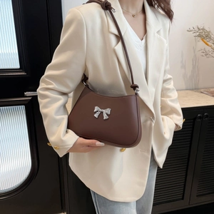 Minimalist brown leather shoulder bag with silver bow detail worn with casual outfit
