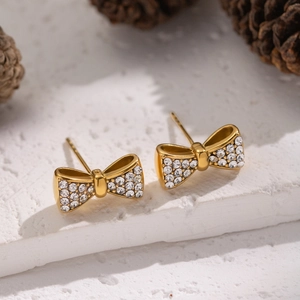 Détail de boucles d'oreilles nœud dorées avec cristaux sur fond blanc texturé élégant
