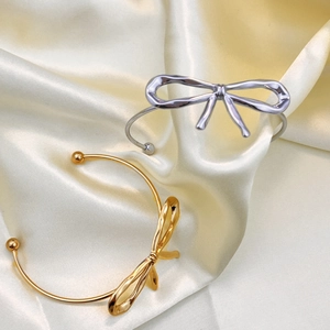 Polished 18K gold and silver bow cuff bracelets on champagne satin fabric background