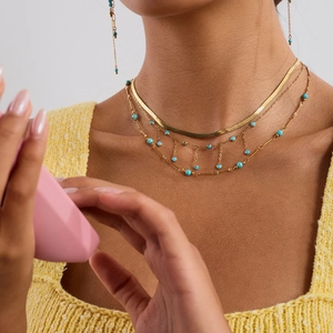 Gros plan d'un collier multicouche en acier doré avec petites perles de turquoise sur modèle