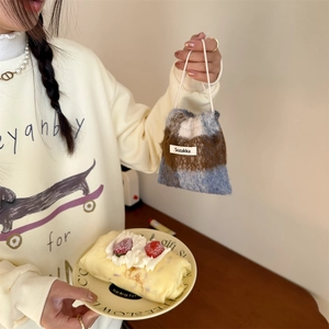 Detail of checkered plush drawstring pouch held by hand in a cozy lifestyle setting