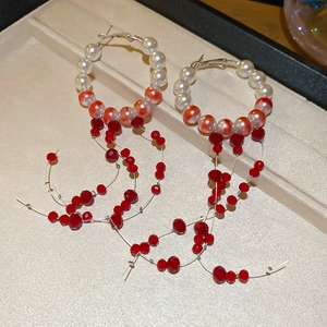 Detailed shot of pearl drop earrings with red beaded tassels in a beige jewelry box
